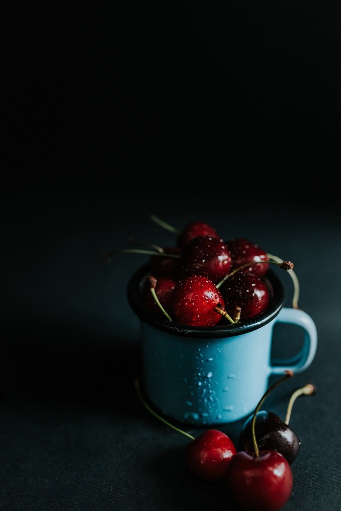 Blue cup filled with fresh cherries on a black background